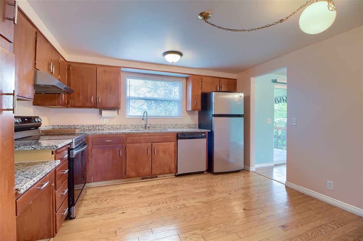 Kitchen featuring stainless steel appliances, wood finish cabinetry, light stone counters, and light wood-style flooring