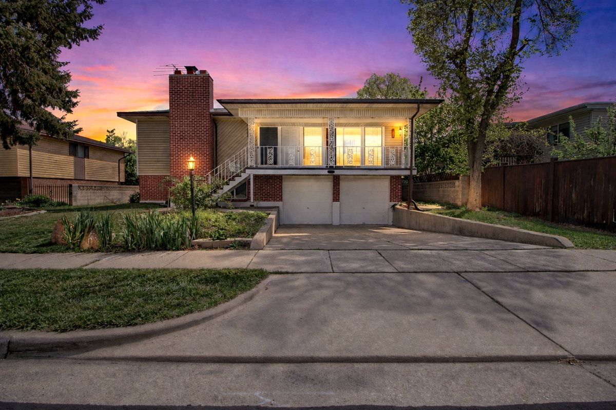View of front facade featuring a garage, brick siding, a chimney, driveway, and covered porch