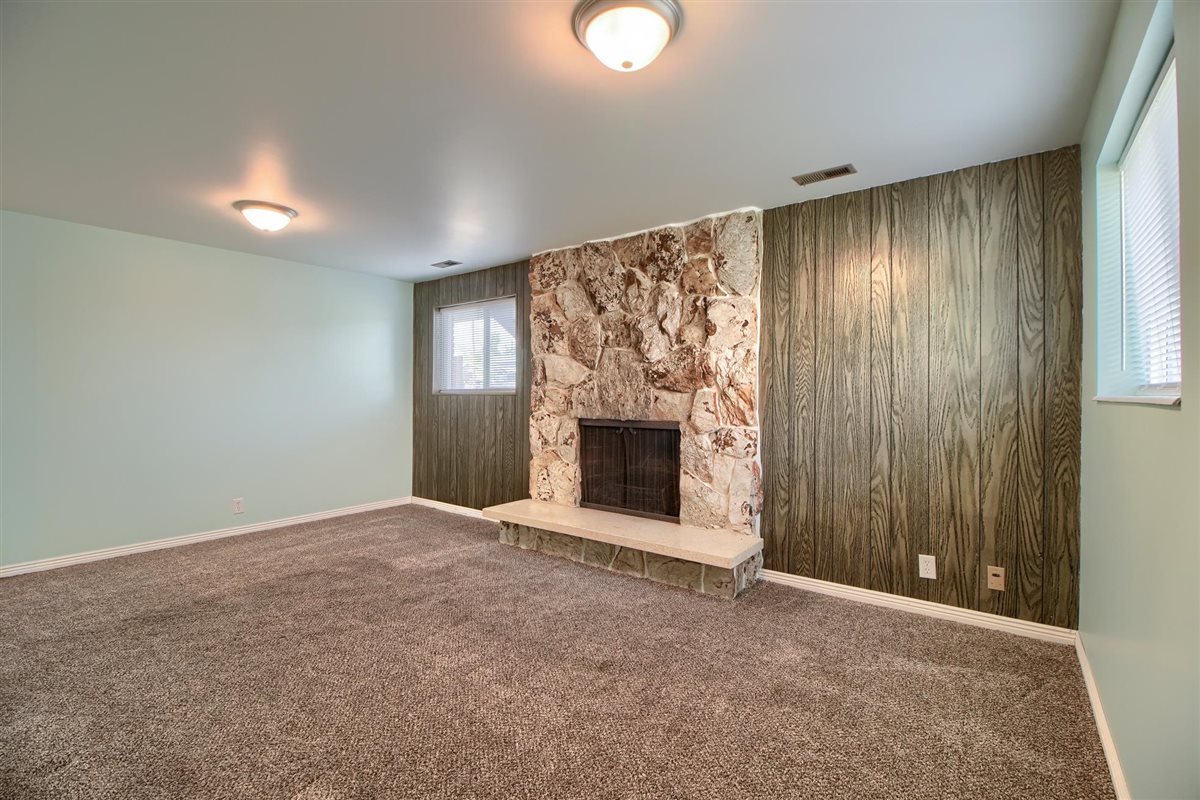 Unfurnished living room featuring wooden walls, carpet flooring, a stone fireplace, and an accent wall
