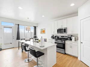 Kitchen featuring stainless steel appliances, a breakfast bar area, a kitchen island with sink, and white cabinetry