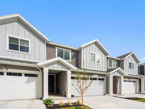 View of front of property with board and batten siding, an attached garage, driveway, and roof with shingles