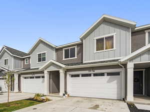 View of front facade with an attached garage, board and batten siding, driveway, and a shingled roof