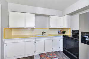 Kitchen with tile counters, black / electric stove, white cabinets, stainless steel refrigerator with ice dispenser, and backsplash