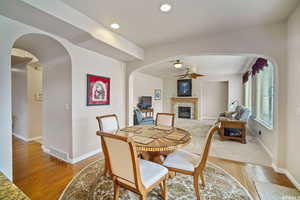 Dining space featuring a ceiling fan, arched walkways, light wood finished floors, a tiled fireplace, and recessed lighting