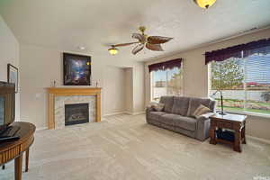 Living area with a ceiling fan, a textured ceiling, light colored carpet, and a tiled fireplace