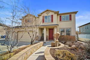 View of front of house with stucco siding, driveway, stone siding, covered porch, and an attached garage