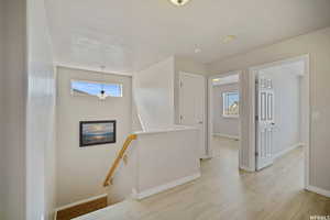 Hall featuring an upstairs landing, light wood-type flooring, and a textured ceiling