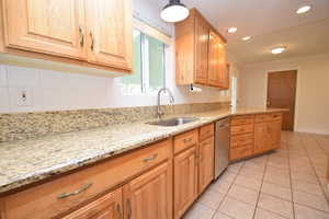 Kitchen with light stone countertops, backsplash, crown molding, dishwasher, and light tile patterned flooring