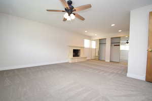 Unfurnished living room featuring ceiling fan, light colored carpet, recessed lighting, and a stone fireplace