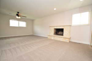 Unfurnished living room with healthy amount of natural light, ceiling fan, light colored carpet, recessed lighting, and a fireplace