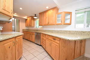 Kitchen featuring light stone counters, stainless steel appliances, glass fronted cabinets, backsplash, and light tile patterned flooring