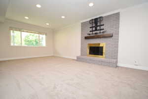 Unfurnished living room with crown molding, carpet flooring, a fireplace, and recessed lighting