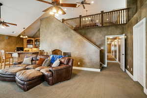 Living room with high vaulted ceiling, ceiling fan, carpet, and stairs