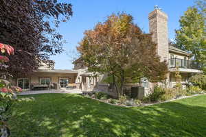 Rear view of house featuring a lawn, a chimney, stucco siding, and a patio area