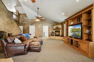 Living room with a tiled fireplace, high vaulted ceiling, built in shelves, ceiling fan, and recessed lighting