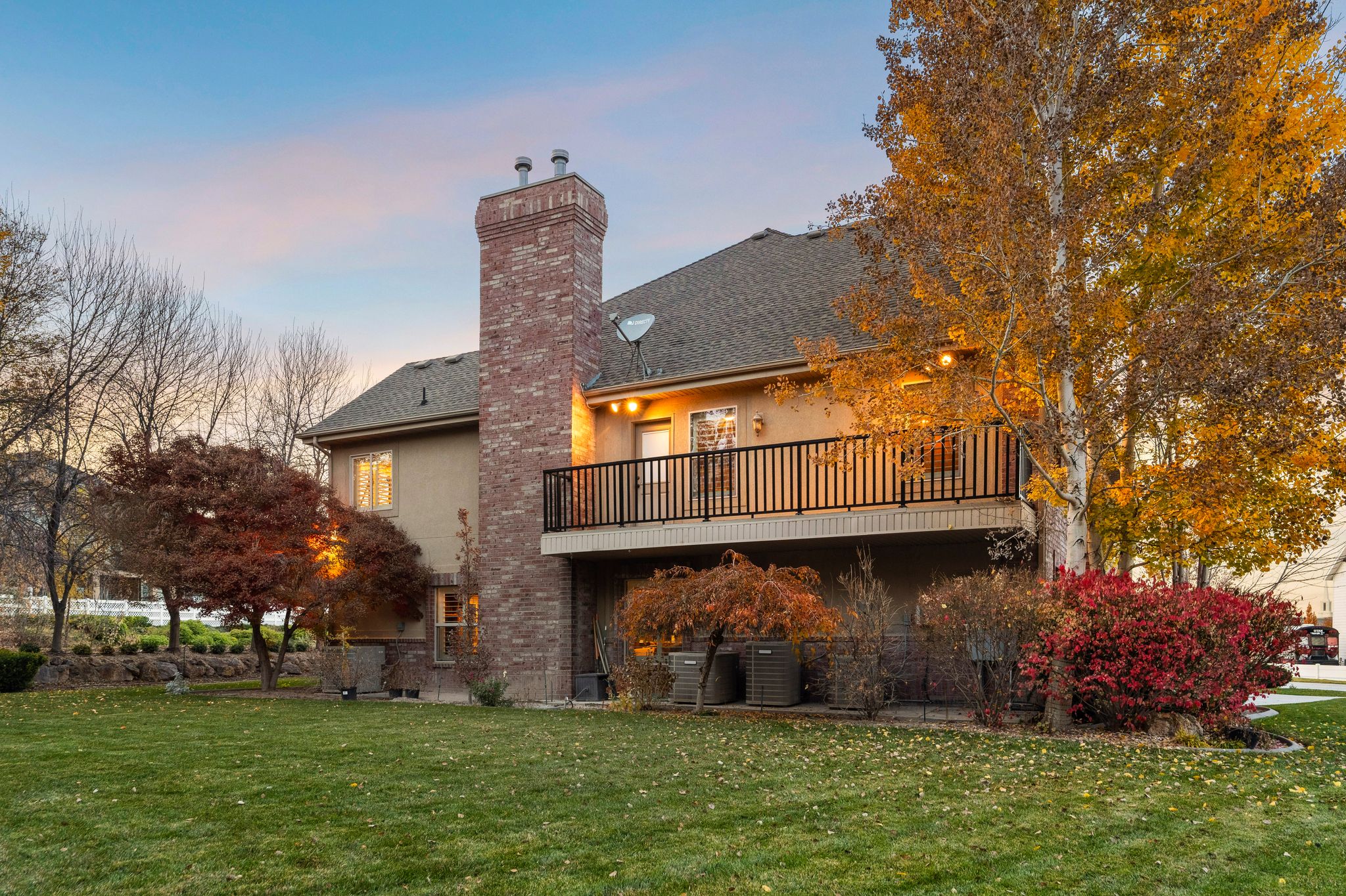 Back of property at dusk featuring a lawn, stucco siding, a chimney, and roof with shingles