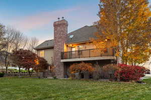Back of property at dusk featuring a lawn, stucco siding, a chimney, and roof with shingles
