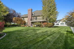 Rear view of house with a yard, a chimney, stucco siding, and a shingled roof