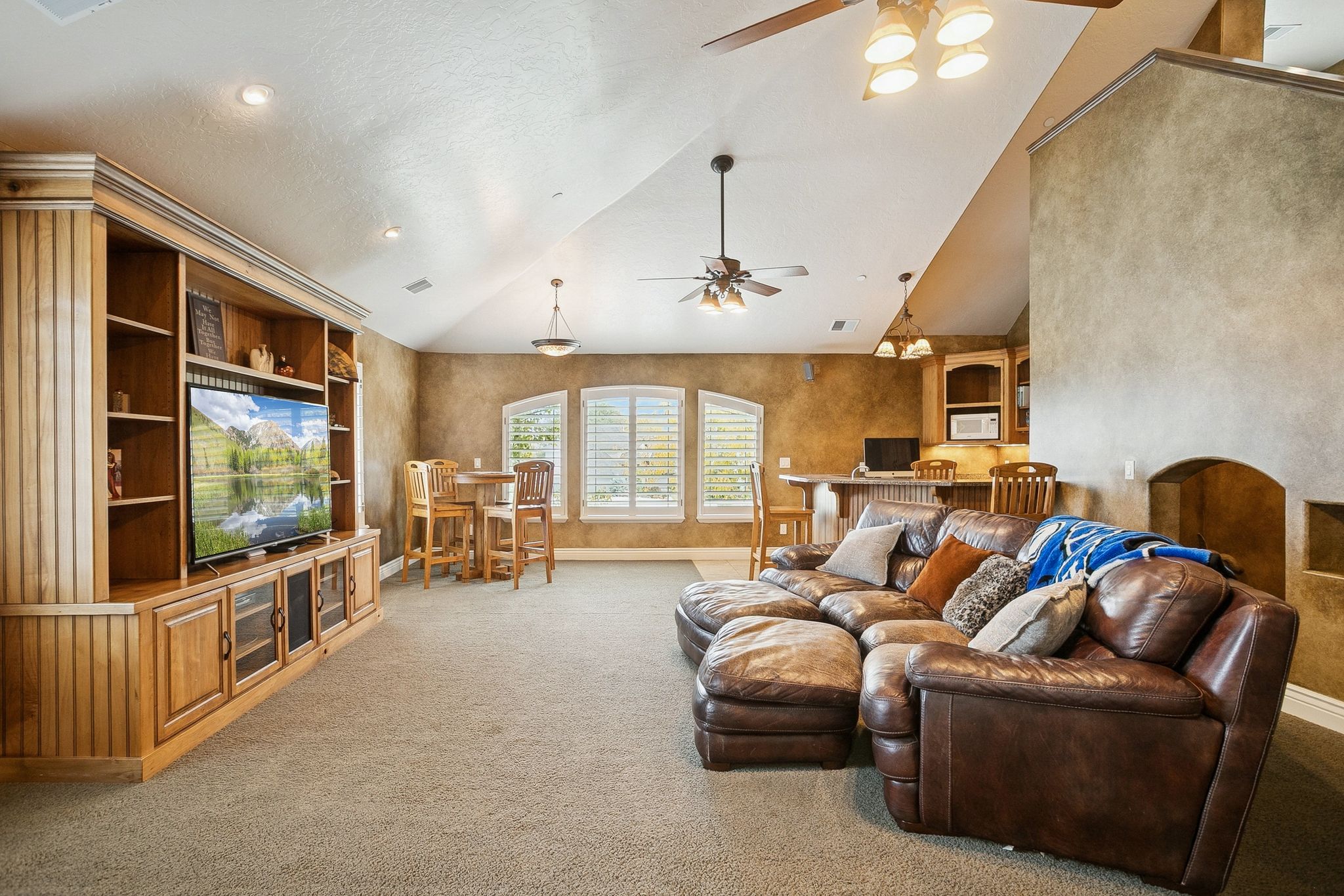 Living area with high vaulted ceiling, ceiling fan, light colored carpet, and arched walkways