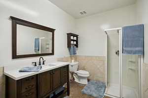 Full bath with wainscoting, tile walls, vanity, a stall shower, and dark tile patterned flooring
