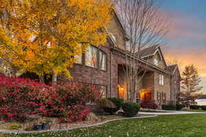 Property exterior at dusk featuring a lawn, covered porch, and brick siding