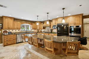 Kitchen featuring brown cabinets, hanging light fixtures, a breakfast bar, stainless steel appliances, and a kitchen island with sink