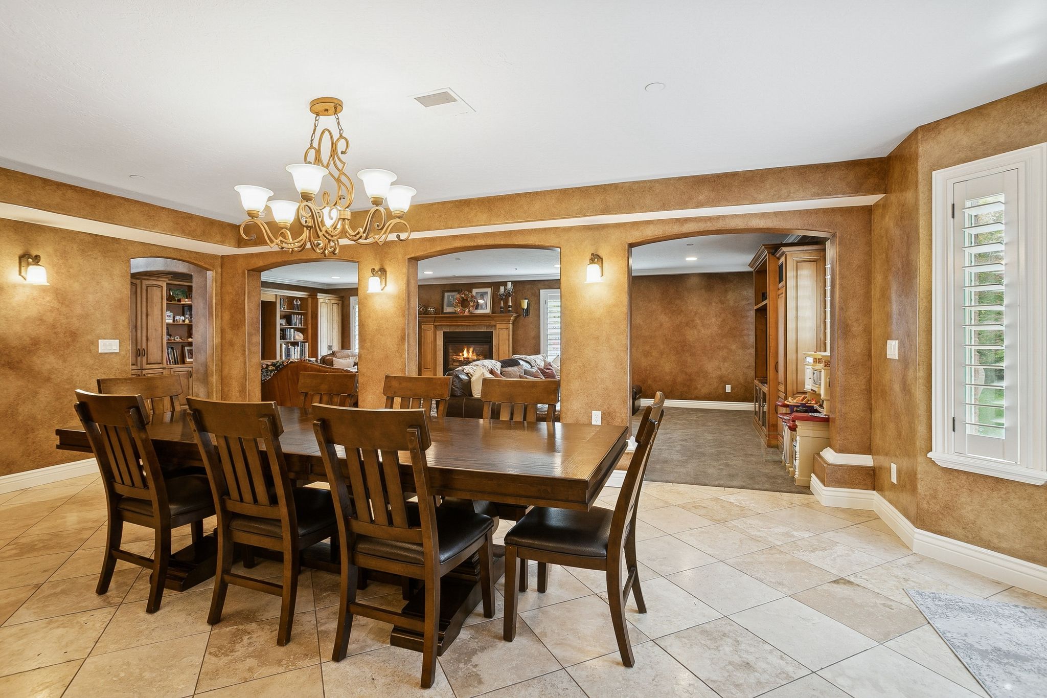Dining area featuring arched walkways, a lit fireplace, light tile patterned flooring, and a chandelier