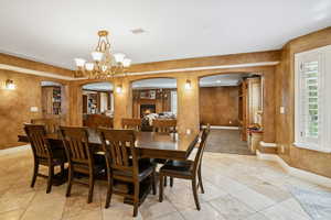 Dining area featuring arched walkways, a lit fireplace, light tile patterned flooring, and a chandelier