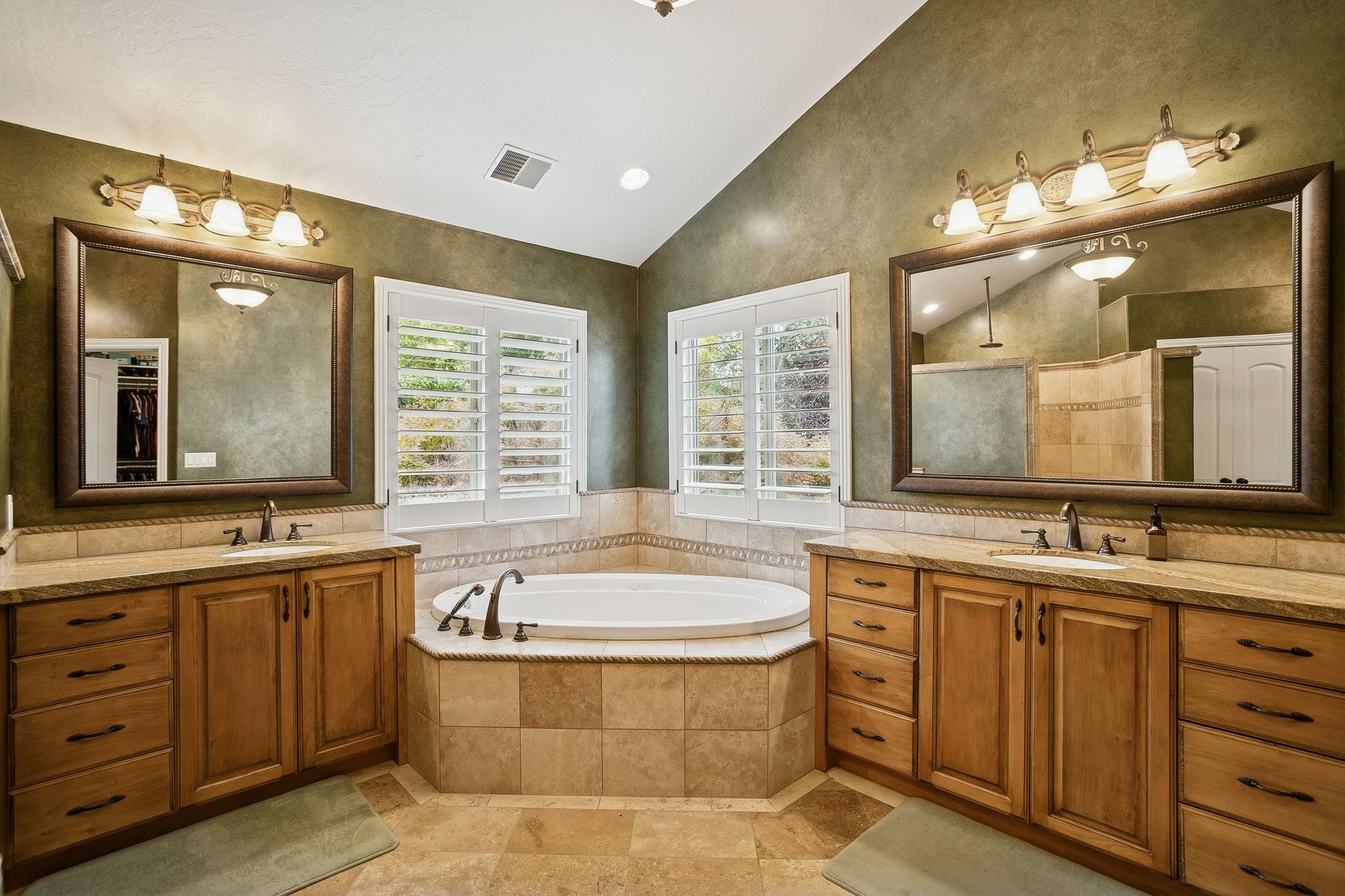 Full bath featuring vaulted ceiling, two vanities, tiled shower, a garden tub, and recessed lighting