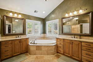 Full bath featuring vaulted ceiling, two vanities, tiled shower, a garden tub, and recessed lighting