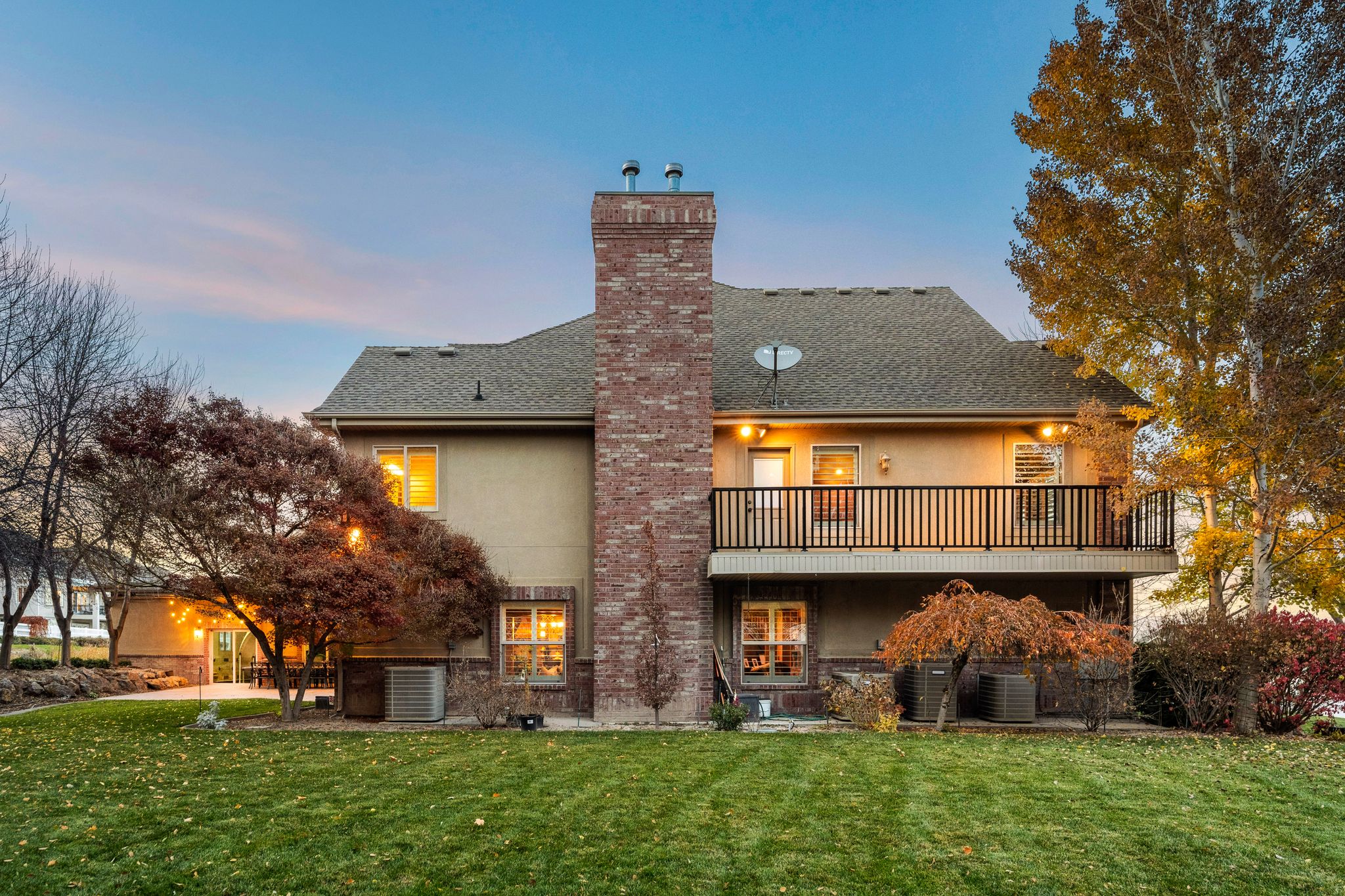 Back of property at dusk with a lawn, a shingled roof, a chimney, and stucco siding
