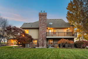 Back of property at dusk with a lawn, a shingled roof, a chimney, and stucco siding
