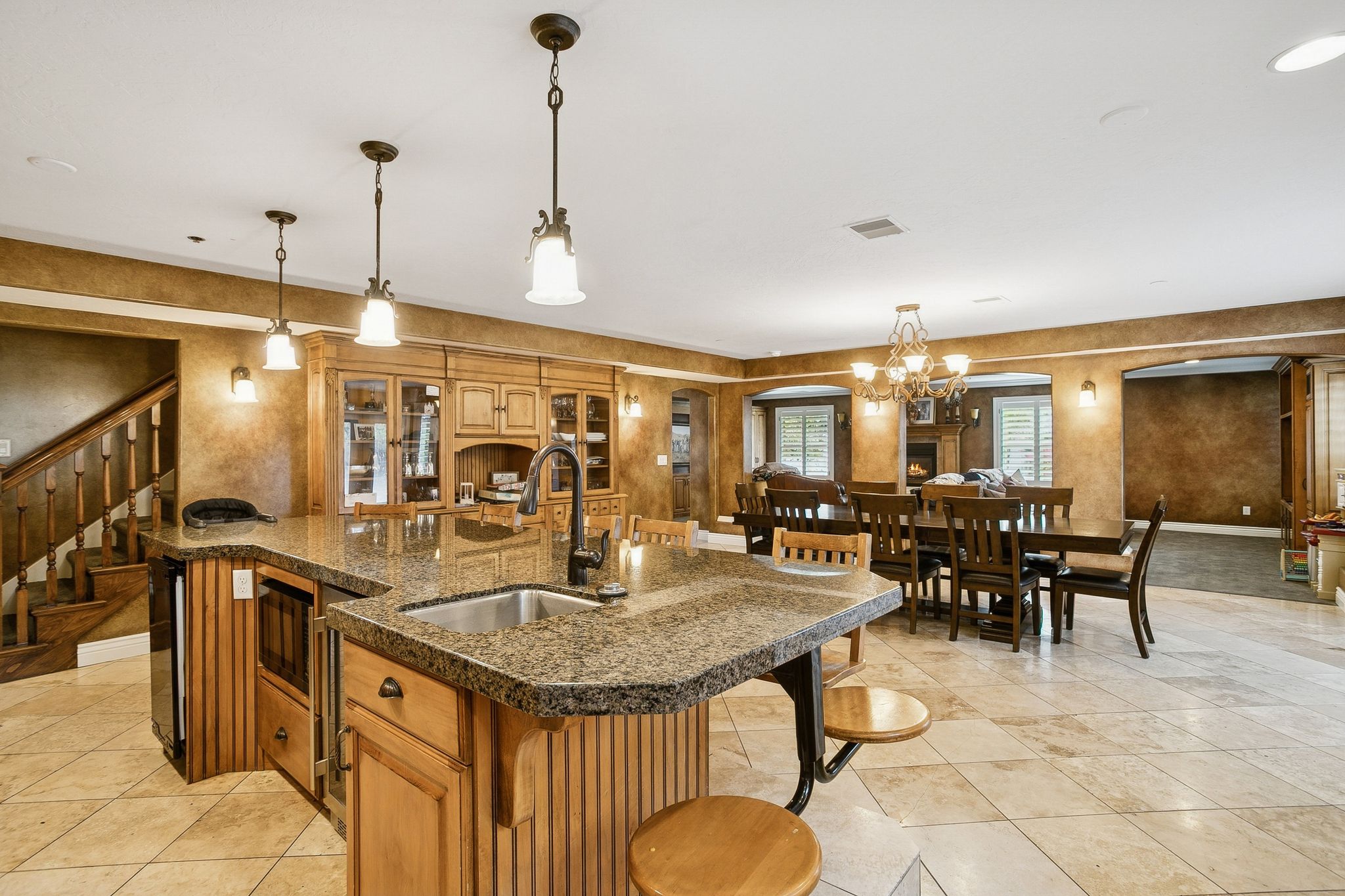 Kitchen featuring brown cabinets, a kitchen bar, a kitchen island with sink, hanging light fixtures, and arched walkways