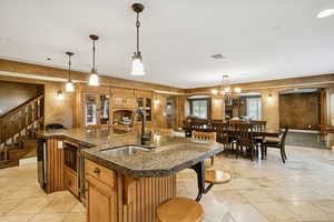 Kitchen featuring brown cabinets, a kitchen bar, a kitchen island with sink, hanging light fixtures, and arched walkways