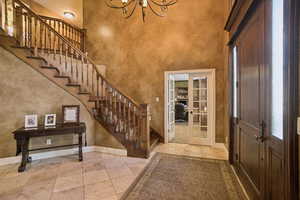 Entrance foyer featuring french doors, a towering ceiling, stairs, a chandelier, and light tile patterned flooring