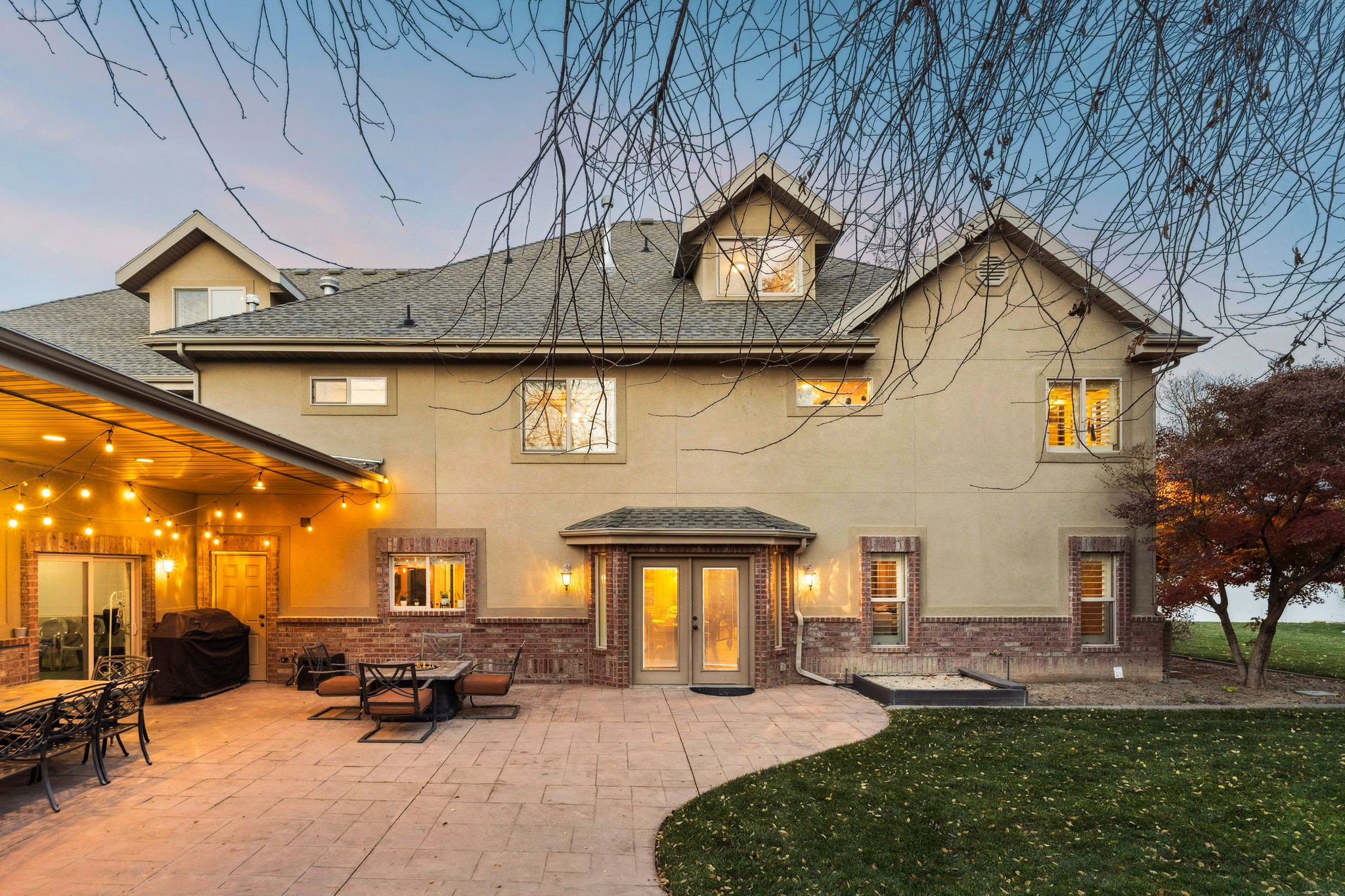 Rear view of house featuring brick siding, a patio, stucco siding, a shingled roof, and a lawn