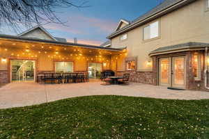 Rear view of property with stucco siding, a patio area, brick siding, a yard, and french doors