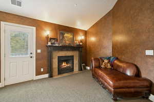 Sitting room featuring lofted ceiling, a tiled fireplace, carpet flooring, and a textured ceiling