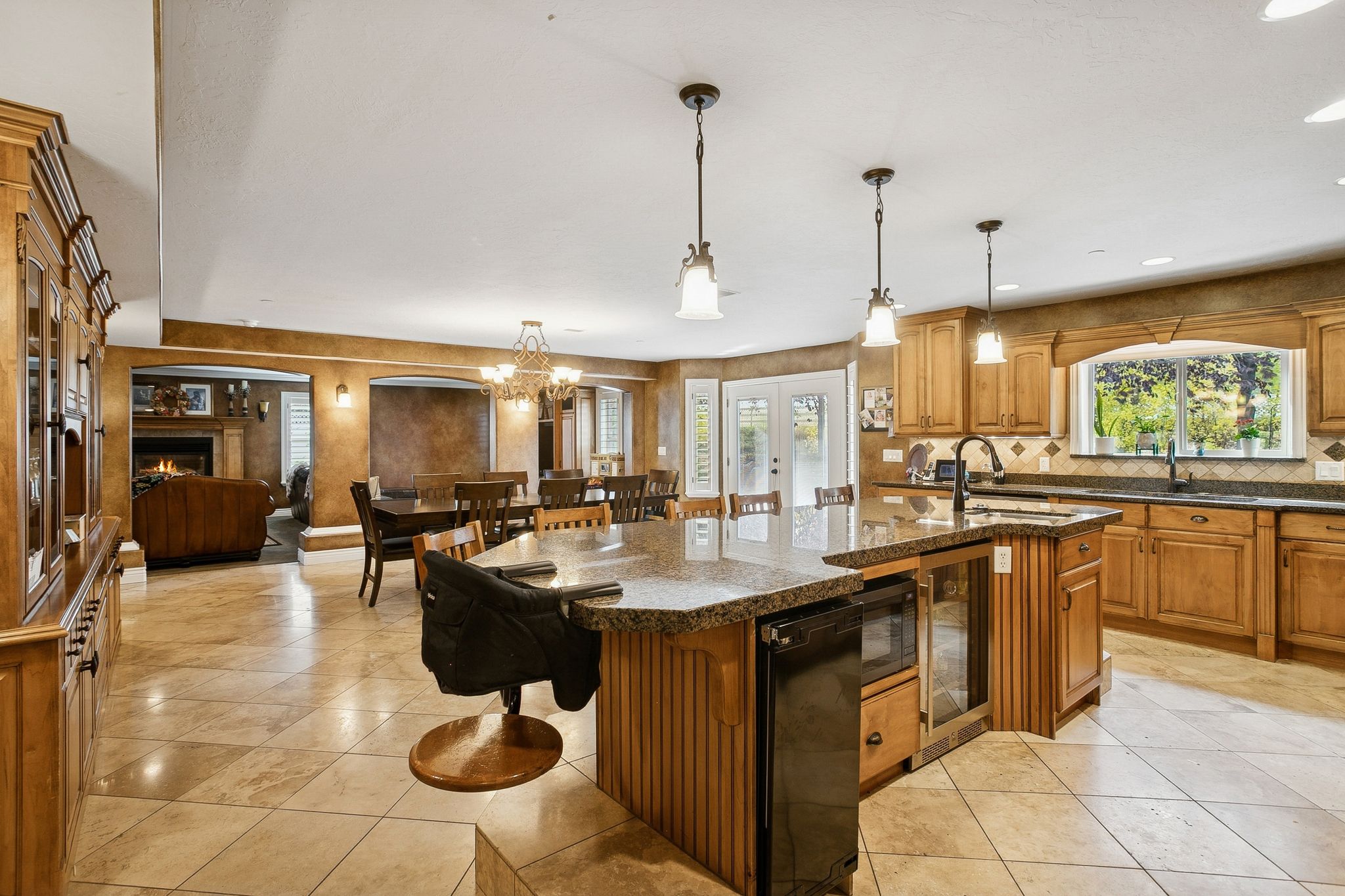 Kitchen with a breakfast bar, brown cabinets, decorative light fixtures, a warm lit fireplace, and beverage cooler