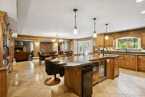 Kitchen with a breakfast bar, brown cabinets, decorative light fixtures, a warm lit fireplace, and beverage cooler