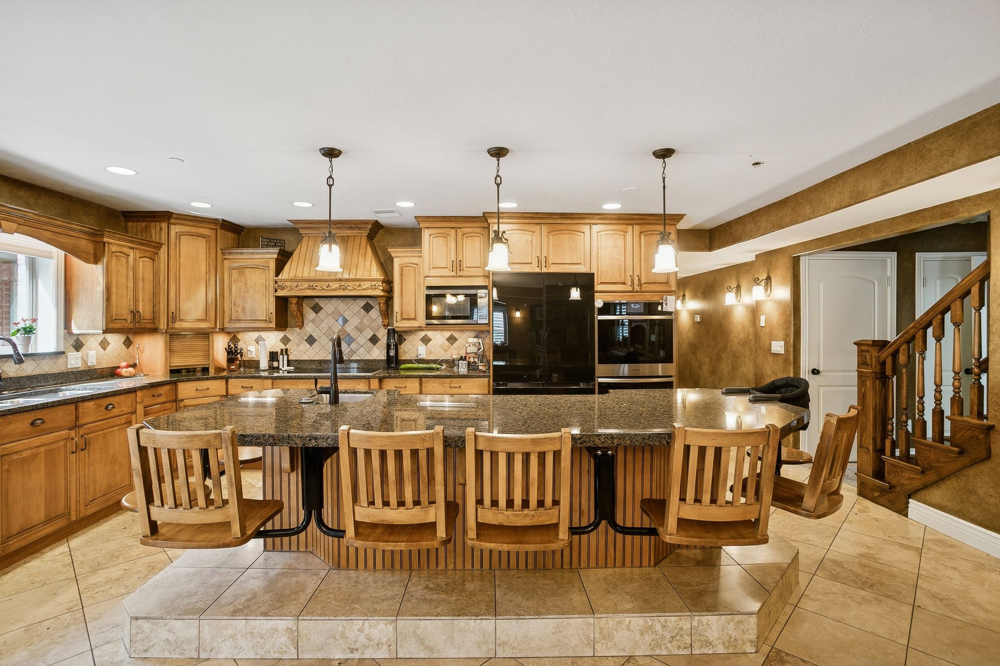 Kitchen featuring brown cabinets, a center island with sink, hanging light fixtures, a breakfast bar, and black appliances