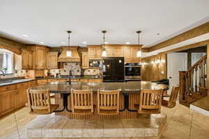 Kitchen featuring brown cabinets, a center island with sink, hanging light fixtures, a breakfast bar, and black appliances