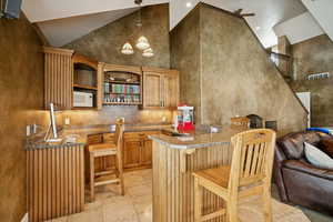 Bar area with high vaulted ceiling, hanging light fixtures, white microwave, open shelves, and brown cabinets