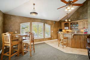 Dining area with light tile patterned floors, light colored carpet, high vaulted ceiling, a ceiling fan, and wet bar