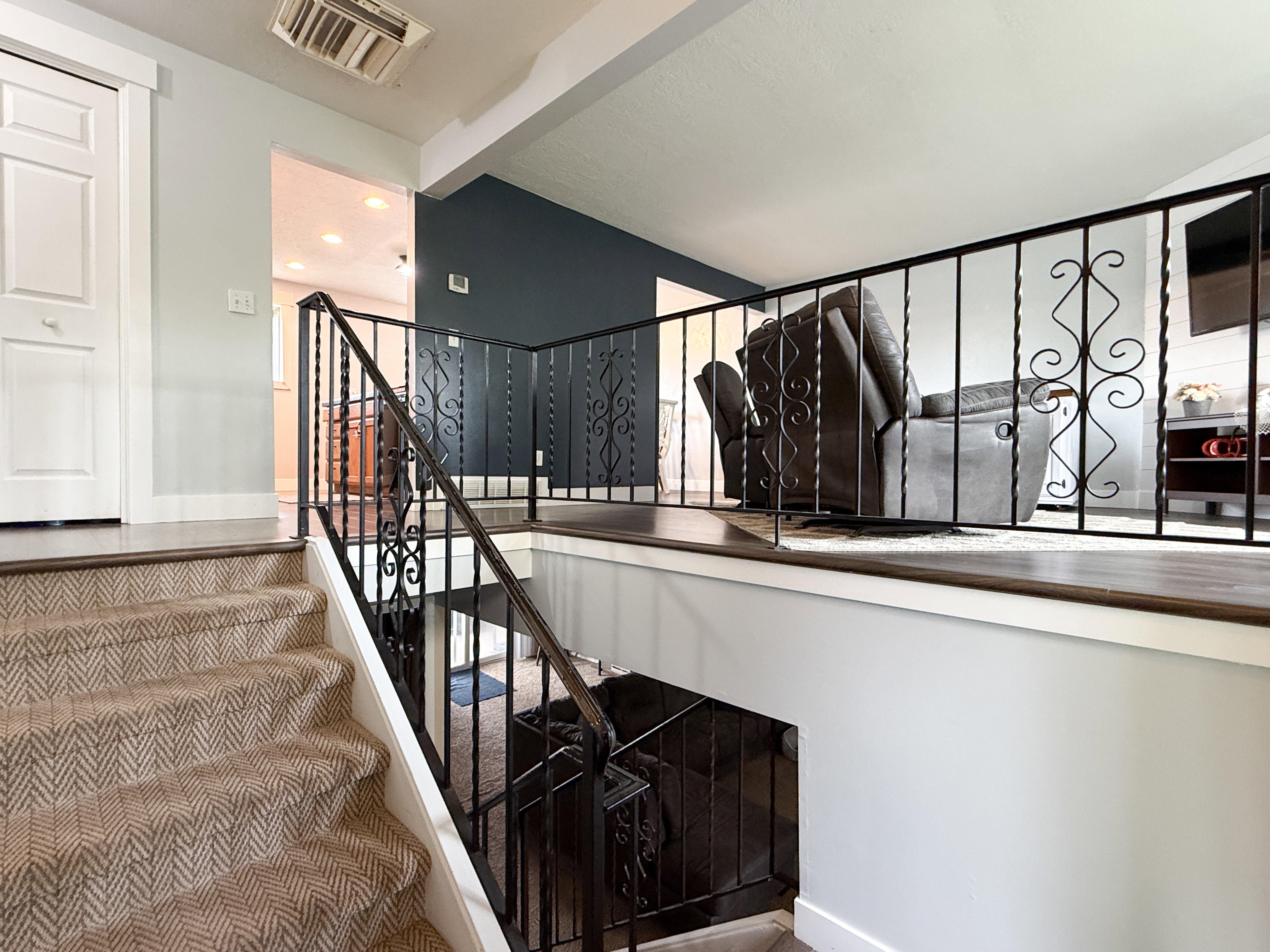 Staircase with patterned carpet treads and white risers, featuring a black wrought iron railing with decorative scrollwork
