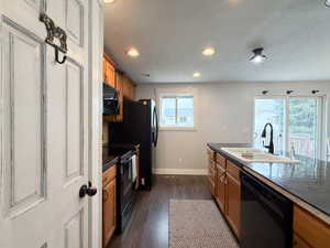 Kitchen featuring dark wood-finish flooring, wood cabinetry, black appliances, recessed lighting, and a black countertop island with an undermount sink and black gooseneck faucet