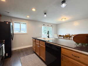 Kitchen featuring wood-finish flooring, recessed lighting, and a center island with an undermount sink and a dark countertop