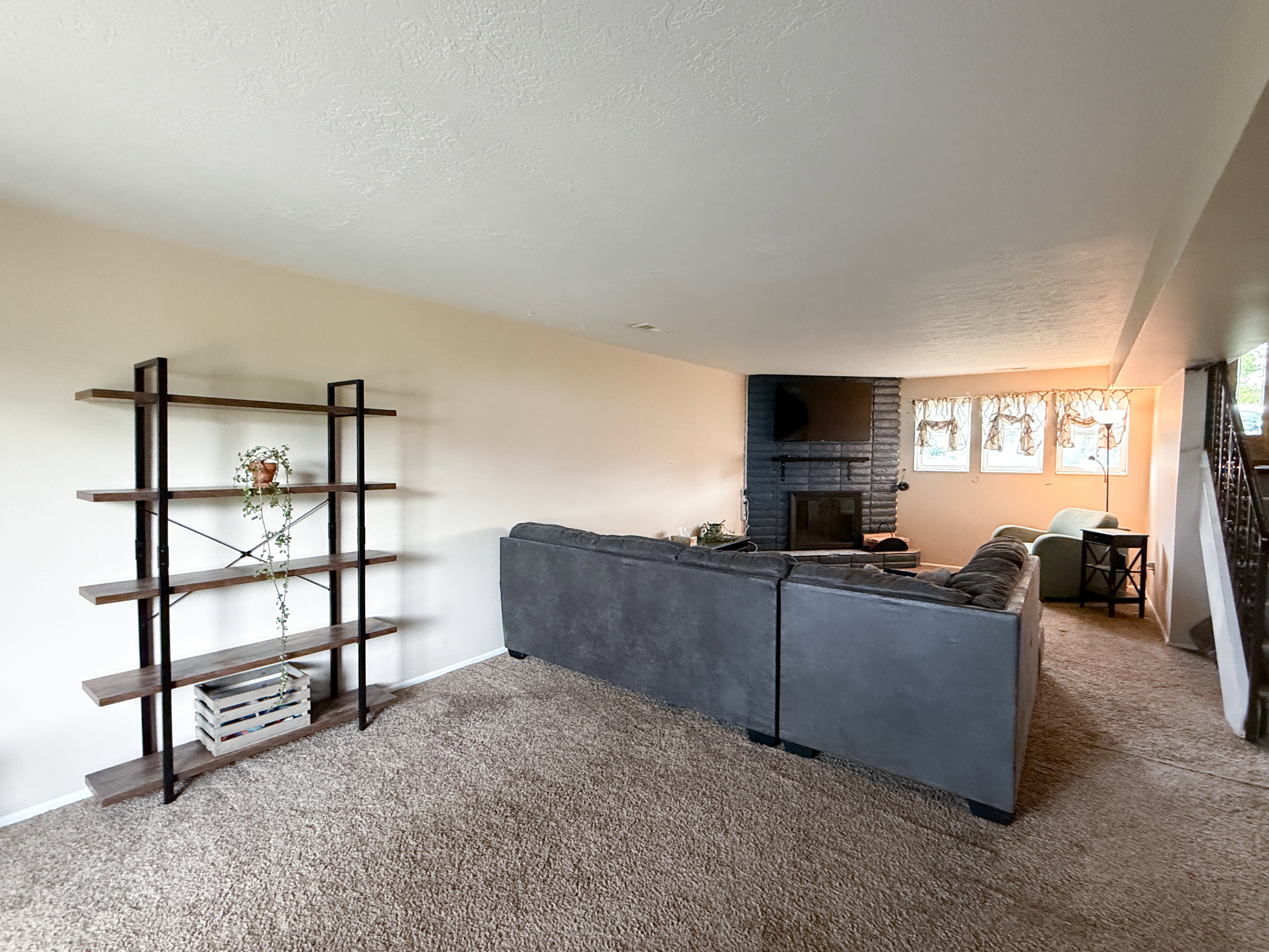 Spacious living area featuring neutral carpeting, light-toned walls, and a prominent dark brick fireplace