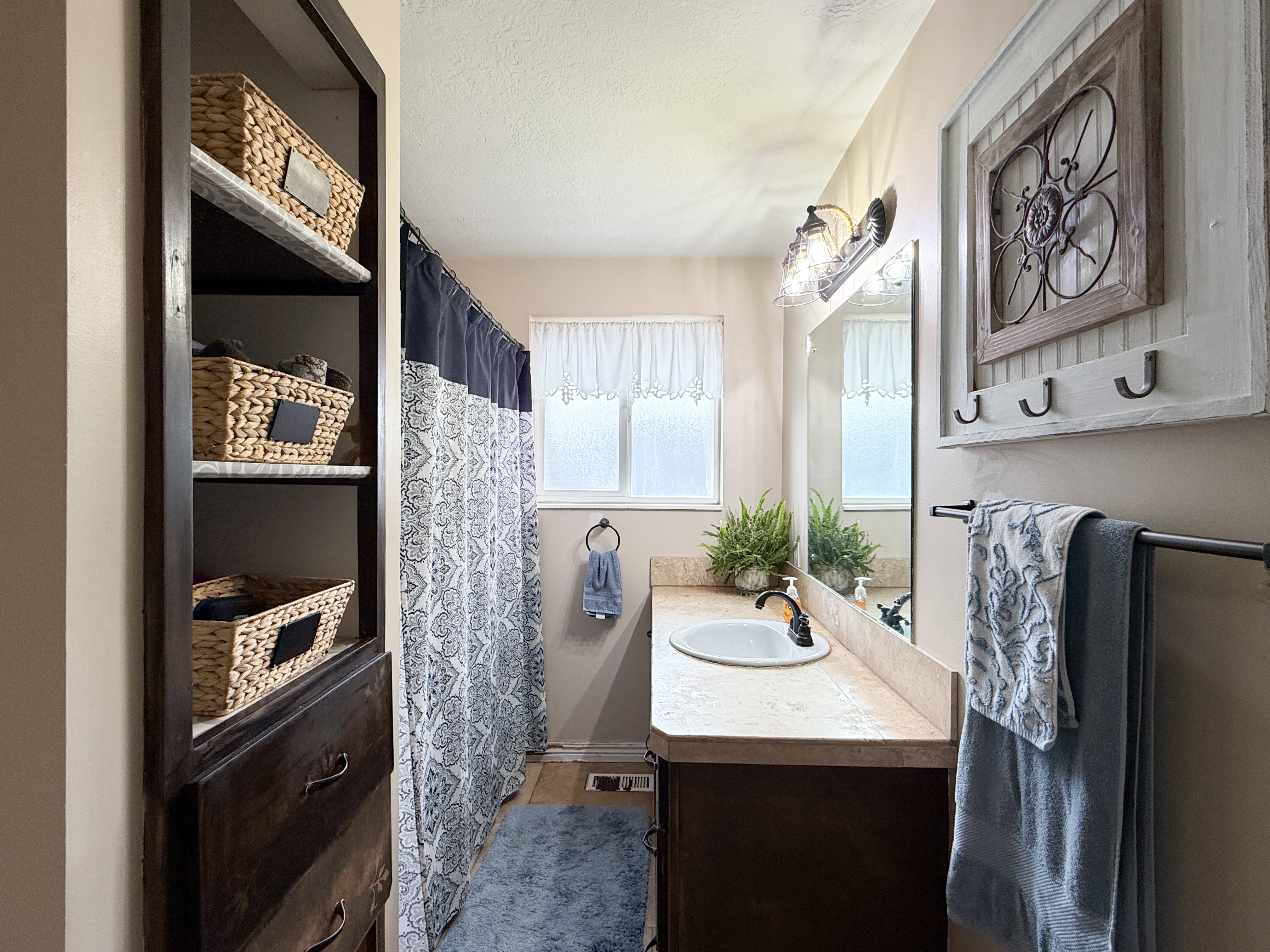 Bathroom featuring a single vanity with an integrated sink, a built-in shelving unit with drawers, wall-mounted light fixtures, a framed mirror, and a wall-mounted towel bar