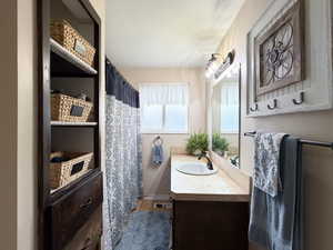 Bathroom featuring a single vanity with an integrated sink, a built-in shelving unit with drawers, wall-mounted light fixtures, a framed mirror, and a wall-mounted towel bar
